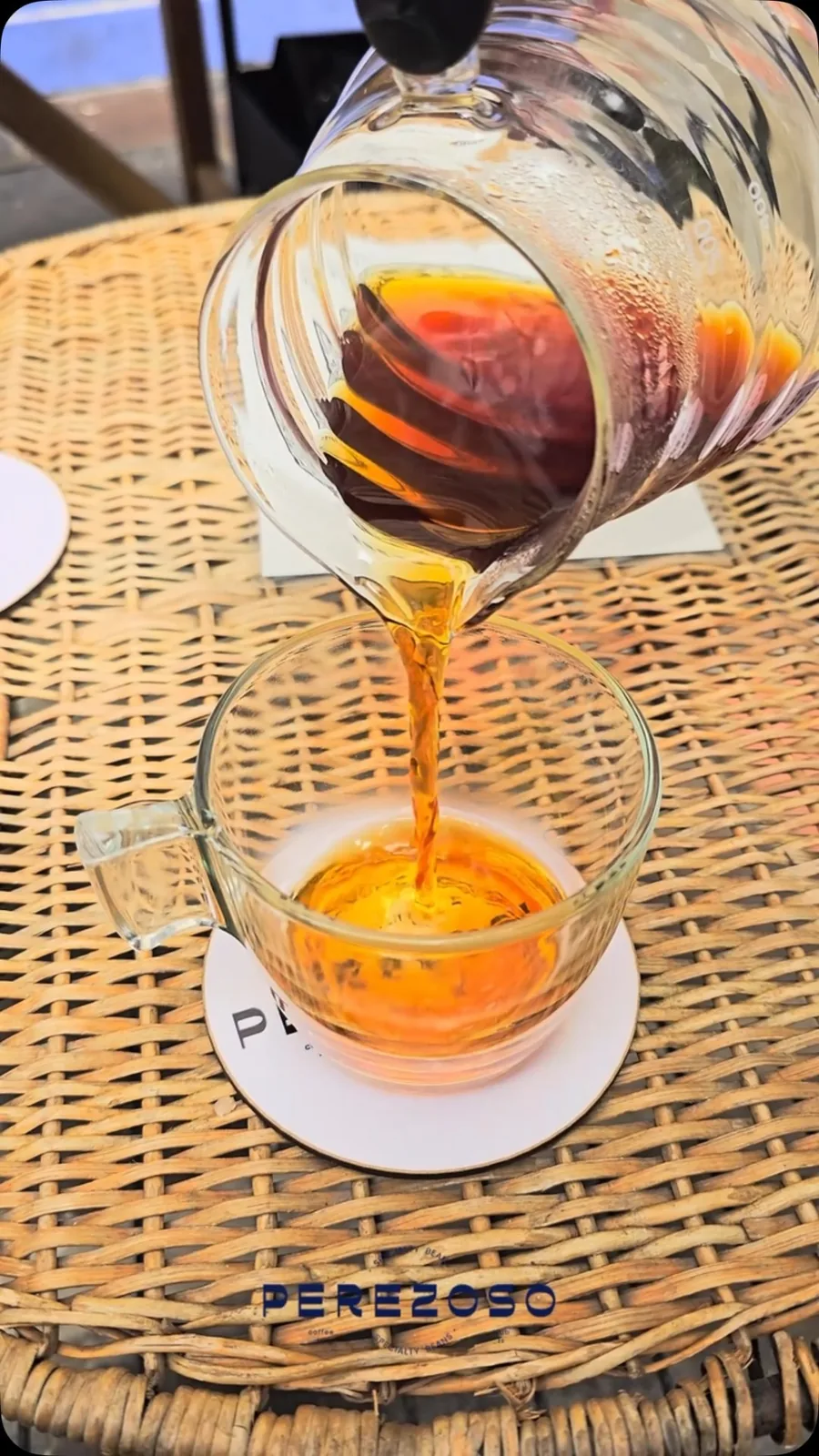 Vertido de café pour over desde jarra de vidrio hacia taza sobre posavasos Perezoso